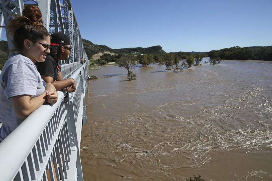Natalie White and Anthony Rodriguez of Odessa stand on a bridge over the flooding, muddy South Llano River in Junction earlier this week. The spring-fed river, usually a narrow ribbon of clear blue/green water, saw its level jump almost 30 feet after as much as a foot of rain fell on the watershed in a few hours. Photo: Tom Reel, Staff / San Antonio Express-News / 2017 SAN ANTONIO EXPRESS-NEWS