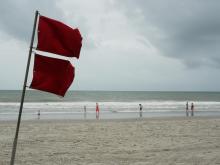 The red hurricane flag flaps in the wind, while families enjoy the ocean at Myrtle Beach before the arrival of Tropical Storm Isaias.